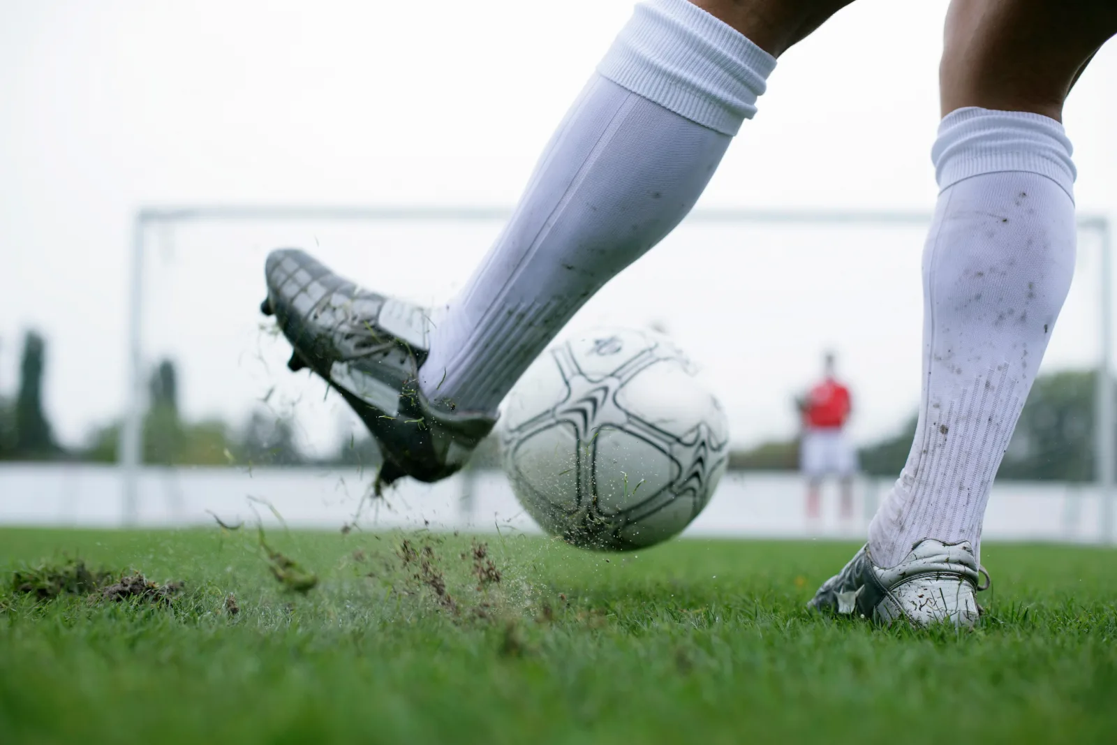 Footballer in white over-the-calf socks and cleats kicking a ball on a grass pitch