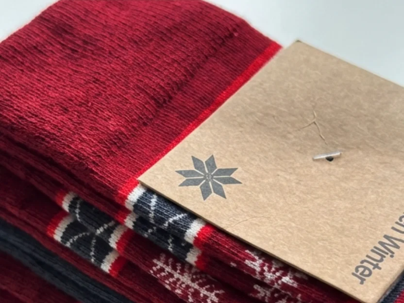 Stack of folded winter socks with intricate snowflake and reindeer jacquard patterns, finished with a kraft-paper hangtag